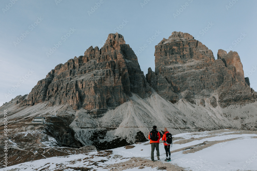 Zwei Personen in roten Jacken vor den drei Zinnen in den Dolomiten. Wandern Tre Cime. Letzte Sonnenstrahlen in den Bergen 5