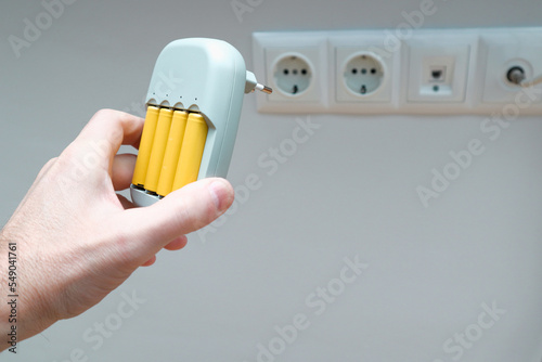 Charger and Batteries in man`s hand. Male hand holding charger with yellow AA batteries, on white background with socket photo