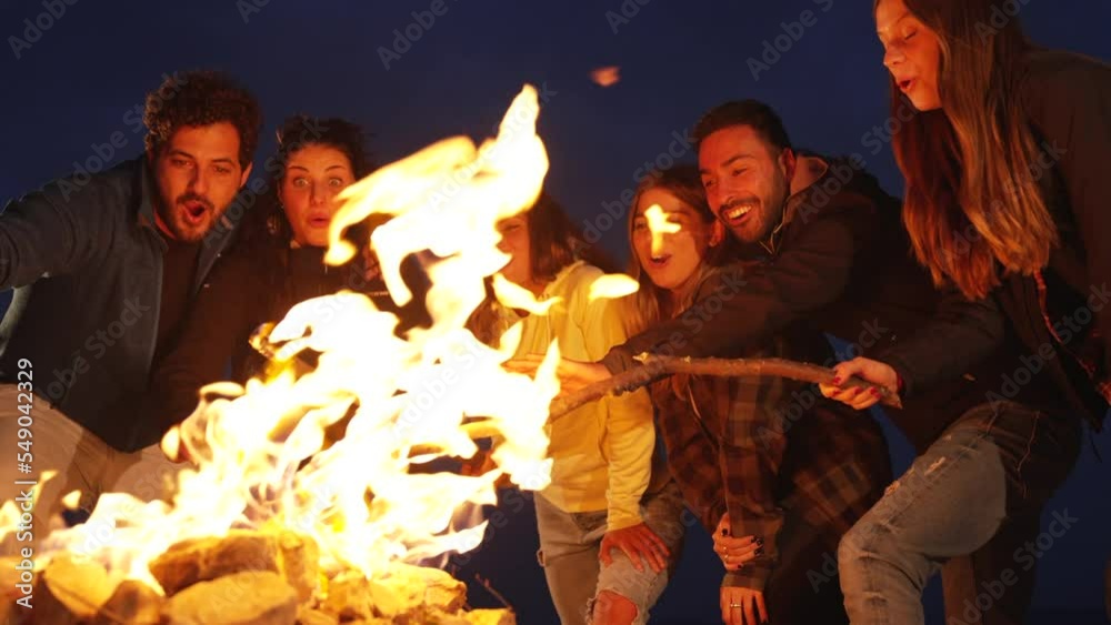 Group of friends having fun together at night party around bonfire - Friendship life style concept with happy people traveler making themselves warm by campfire at dusk night time Group of friends having fun together at night party around bonfire - Friendship life style concept with happy people traveler making themselves warm by campfire at dusk night time