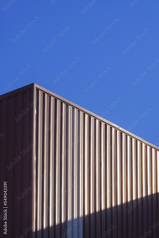 Brown Corrugated Steel Wall of Warehouse Building with sunlight on surface with blue clear sky background in Vertical frame