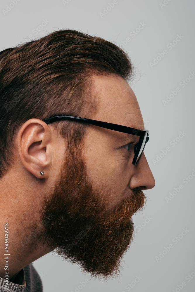 Obraz premium Side view of bearded man in eyeglasses looking away isolated on grey.
