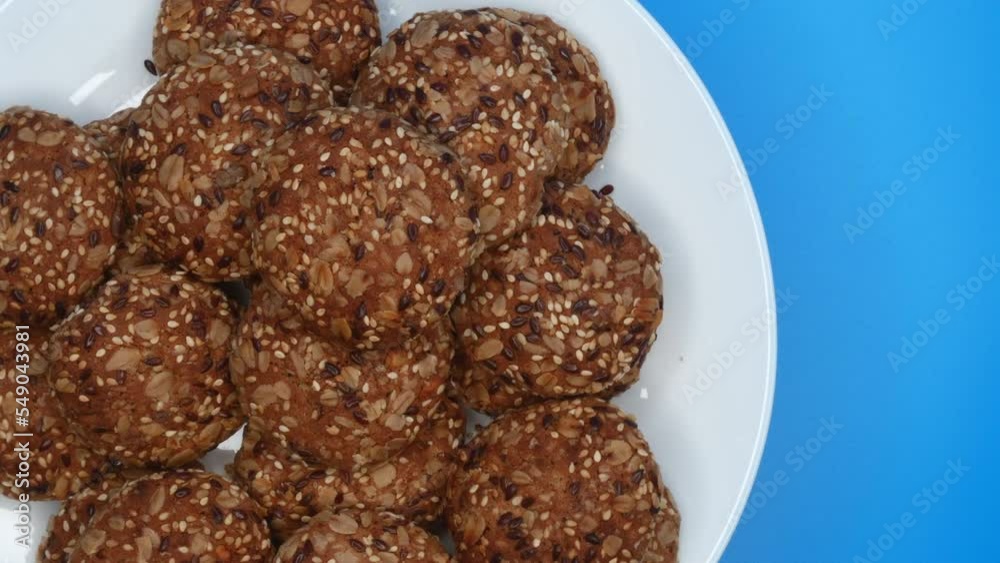 Rotation Of Oatmeal Cookies With Sesame Seeds On A Plate On A Blue Background On The Left Side. Top View. Close Up. 4k, ProRes
