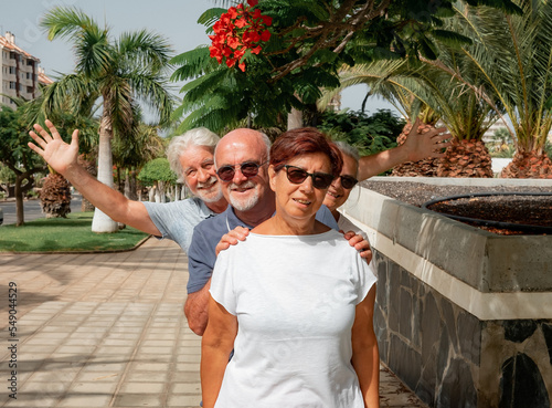 Cheerful group of four seniors in the park joking around lining up behind each other - concept of active and positive seniors during retirement