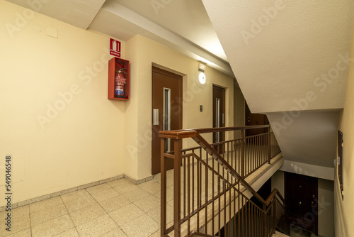 Landing of a residential apartment house with a staircase with light terrazzo floors, red painted metal railings and double elevators