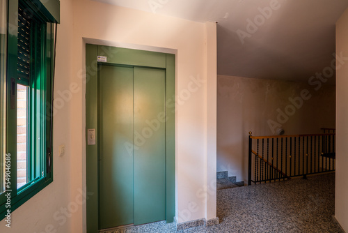 Landing of a residential apartment building with granite floors  black metal railing with wood and a green painted elevator