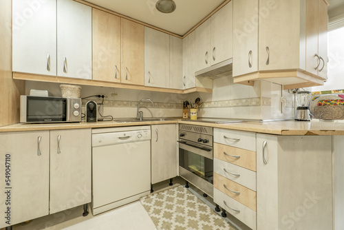 Corner of a kitchen covered with white furniture combined with wood-colored drawers, integrated appliances and tile border on the walls