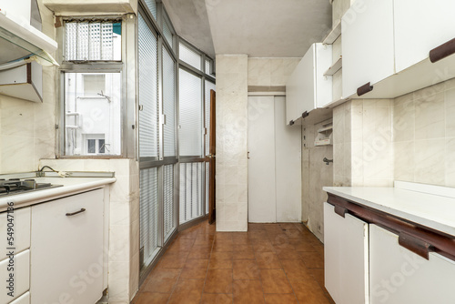 Old kitchen of a house with white furniture  aluminum partition and translucent glass and brown stoneware floors