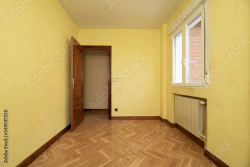 Small empty room with herringbone parquet flooring  niche under window for aluminum radiator and yellow painted walls