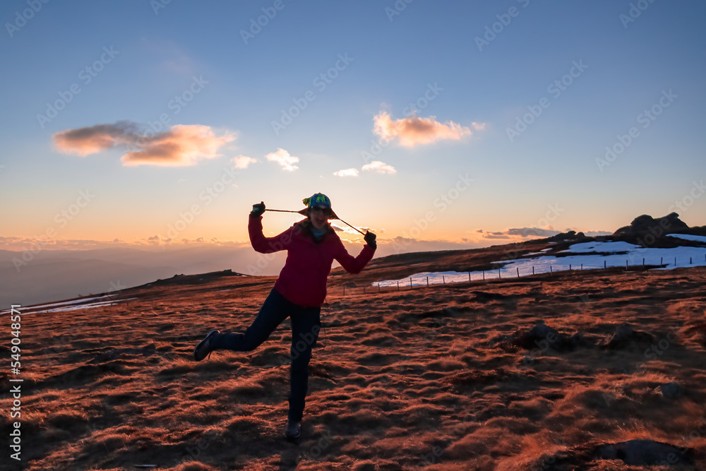 Silhouette of woman holding her winter hat during sunset on mountain peak Ladinger Spitz, Saualpe, Lavanttal Alps, Carinthia, Austria, Europe. Warm atmosphere, inspiration, goal seeking concept