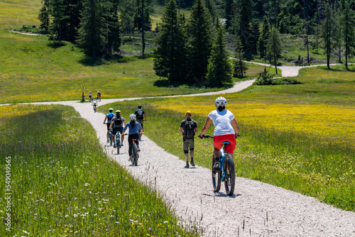 a group of mountain bike cyclist on a gravel road between green meadows in the Dolomites