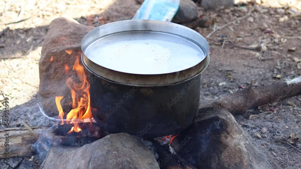 Open fire cooking in an Indian village An aluminum utensil on a temporarily made fire oven. Rural kitchen using bio wood fuel for cooking. plate filled with water is placed on top of the utensil. Open fire cooking in an Indian village An aluminum utensil on a temporarily made fire oven. Rural kitchen using bio wood fuel for cooking. plate filled with water is placed on top of the utensil.