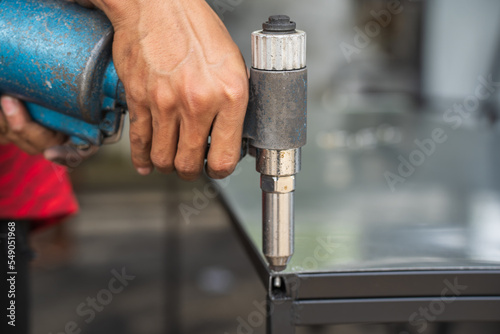 An industrial worker uses an air pop rivet gun to fasten workpieces with aluminum nails.