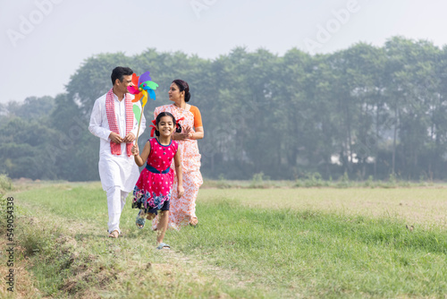 Happy parents with cute little girl running carefree and having fun with colorful pin wheel.