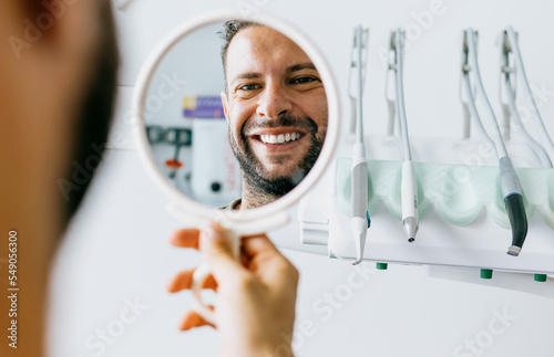 Satisfied man looks in the mirror and smiles after treatment at the dentist