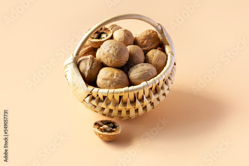 A beige basket with walnuts on an orange background and half a cracked walnut on the table