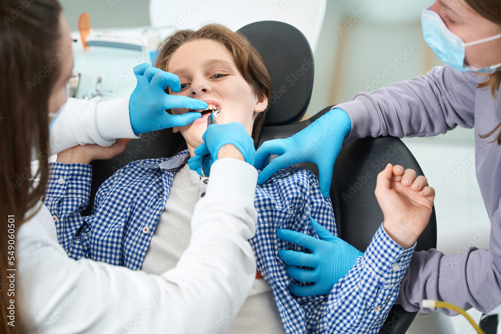 Woman dentist removes tooth to young patient with special tool Woman dentist removes tooth to young patient with special tool