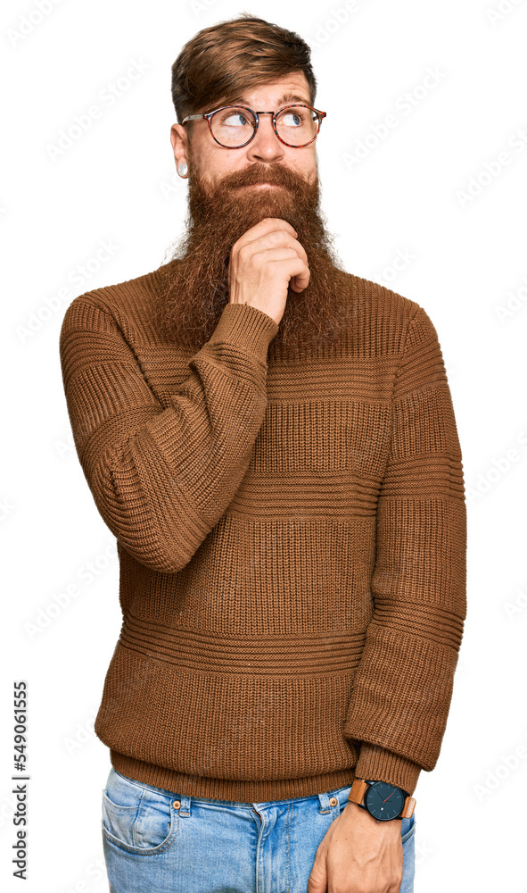 Young irish redhead man wearing casual clothes and glasses with hand on chin thinking about question, pensive expression. smiling and thoughtful face. doubt concept. Young irish redhead man wearing casual clothes and glasses with hand on chin thinking about question, pensive expression. smiling and thoughtful face. doubt concept.
