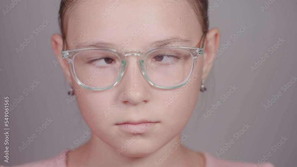 Funny close-up of serious teen girl with glasses strabismus squints her eyes looking at camera. Funny close-up of serious teen girl with glasses strabismus squints her eyes looking at camera.