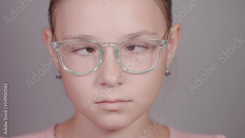 Funny close-up of serious teen girl with glasses strabismus squints her eyes looking at camera. photo