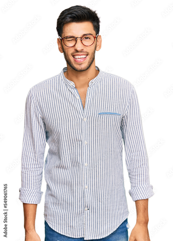 Young handsome man wearing casual clothes and glasses winking looking at the camera with sexy expression, cheerful and happy face. Young handsome man wearing casual clothes and glasses winking looking at the camera with sexy expression, cheerful and happy face.