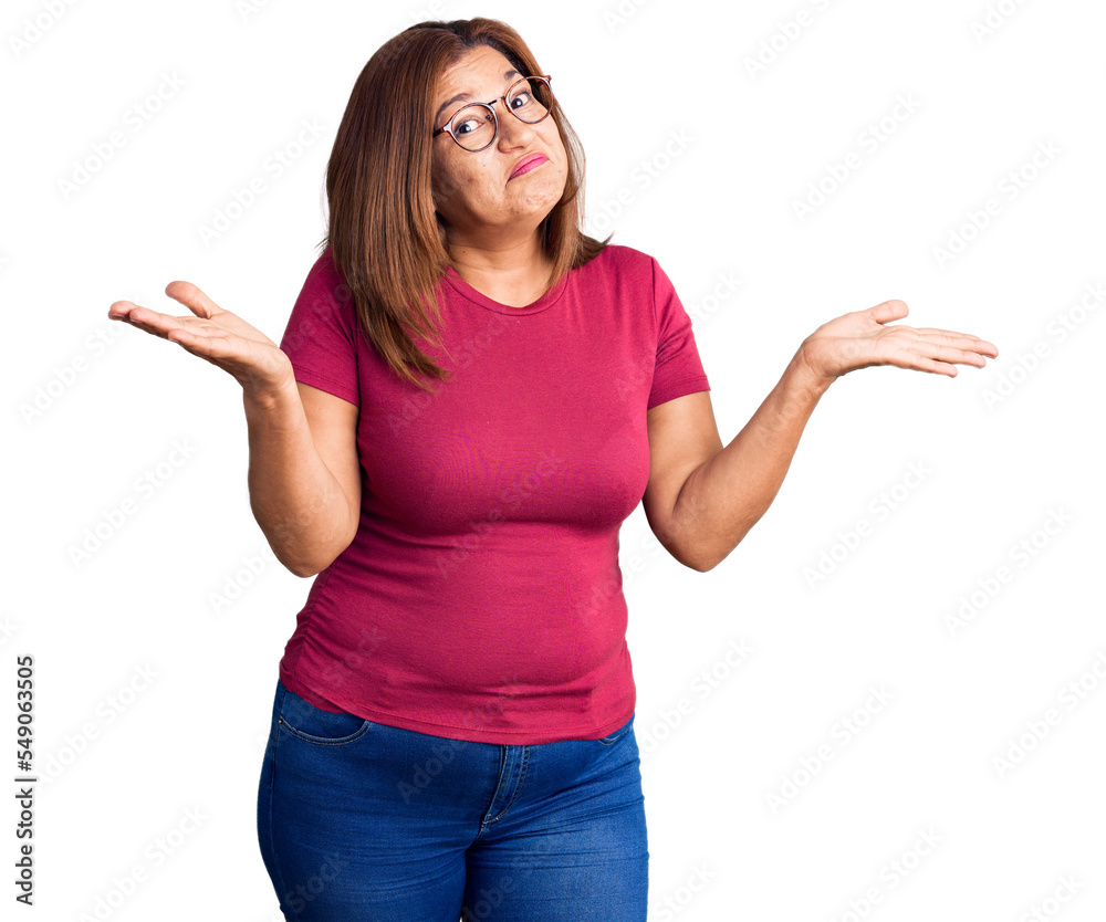 Middle age latin woman wearing casual clothes and glasses clueless and confused expression with arms and hands raised. doubt concept. Middle age latin woman wearing casual clothes and glasses clueless and confused expression with arms and hands raised. doubt concept.