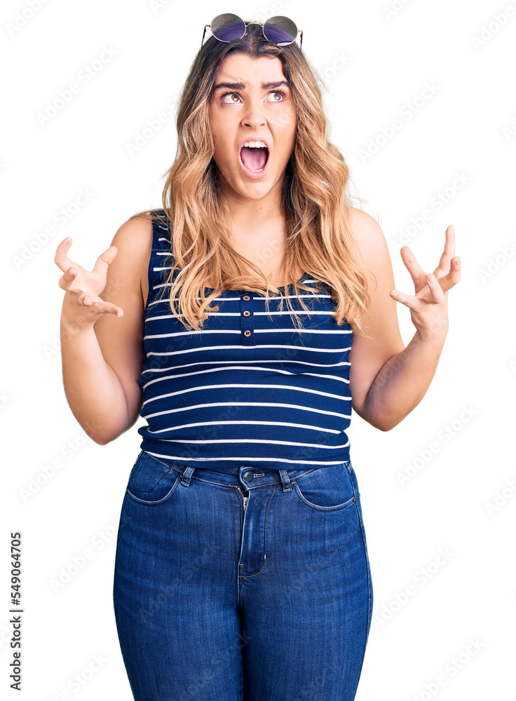 Young caucasian woman wearing casual clothes and sunglasses crazy and mad shouting and yelling with aggressive expression and arms raised. frustration concept. Young caucasian woman wearing casual clothes and sunglasses crazy and mad shouting and yelling with aggressive expression and arms raised. frustration concept.