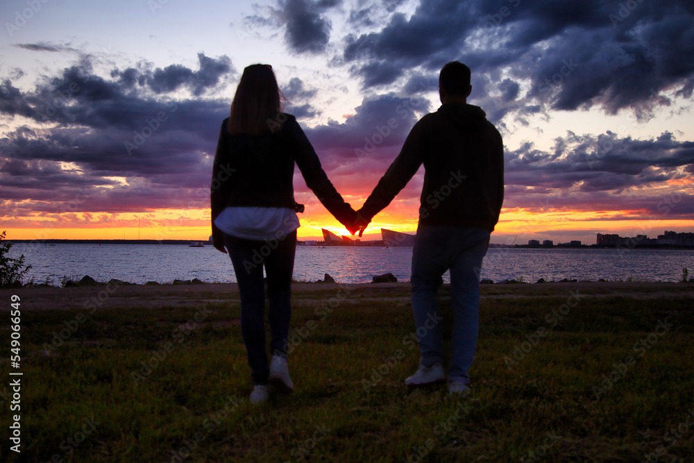 Young couple holding hands, woman and man together spending summertime walking at sunset background. Caucasian couple enjoy leisure activity, outdoors. Concept of family relationship. Copy space