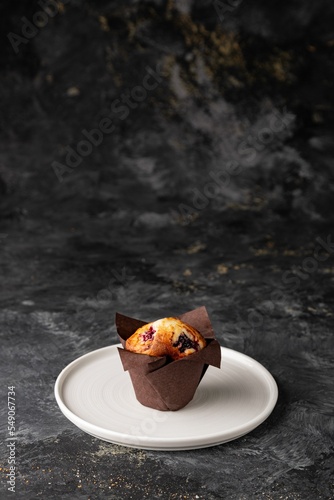 Vertical closeup of a blueberry raspberry vanilla muffin on a white plate on a dark background