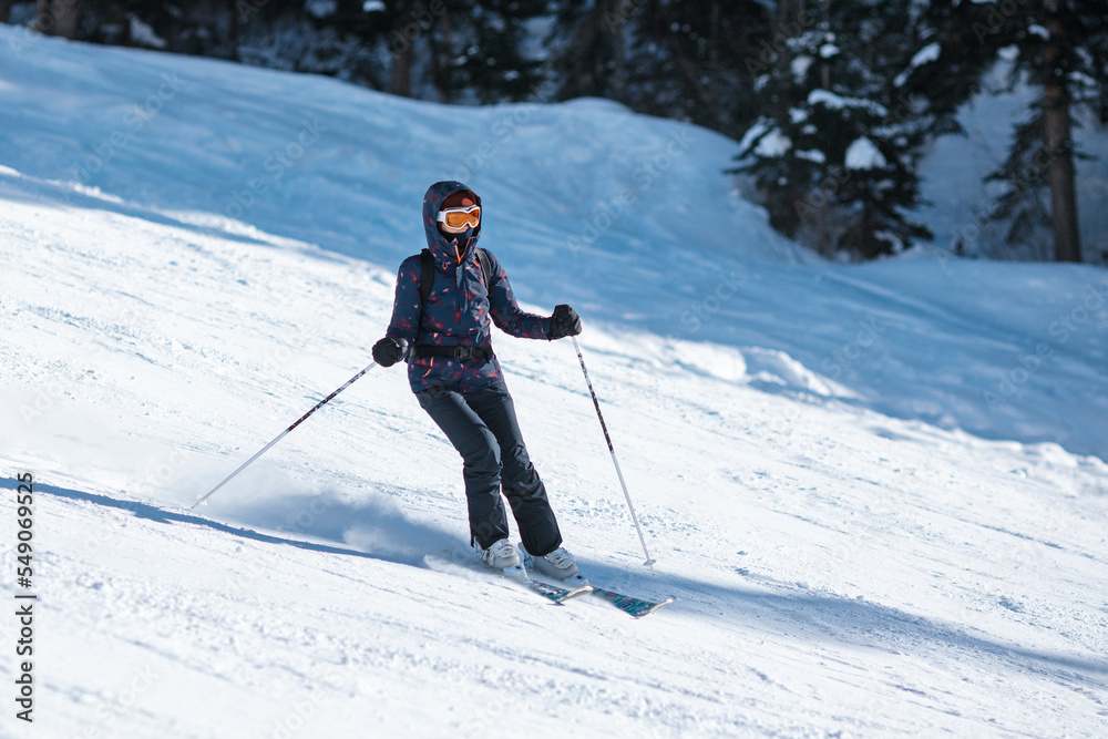 Amateur female skier sliding down the slope on a sunny day at a mountain resort.