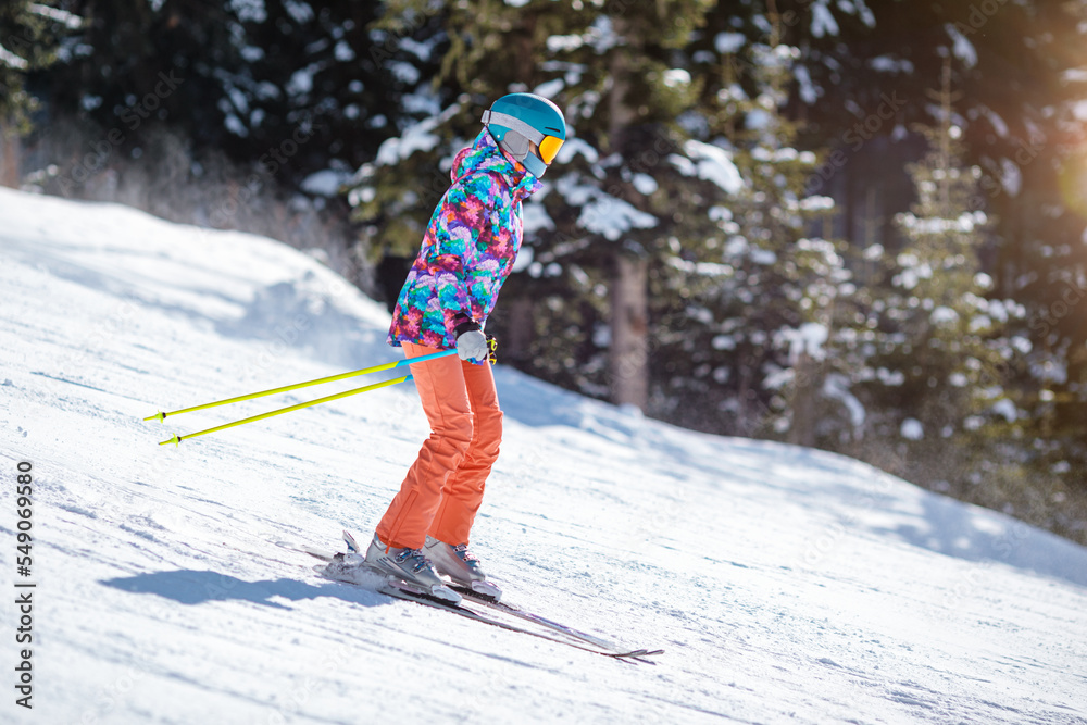 Young skier learning to slide down the slope on a sunny day at a mountain resort.