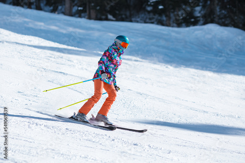 Young skier in bright clothes sliding down the slope on a sunny day at a mountain resort.