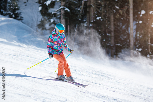 Obraz na płótnie Young skier in bright clothes sliding down the slope on a sunny day at a mountain resort. w salonie