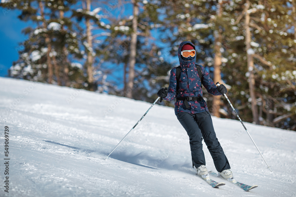 Amateur female skier sliding down the slope on a sunny day at a mountain resort.