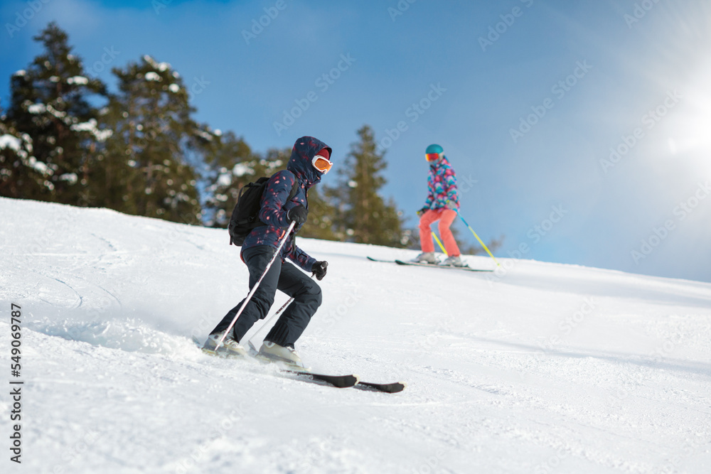 Two young female skiers sliding down the slope on a sunny day at a ski resort.