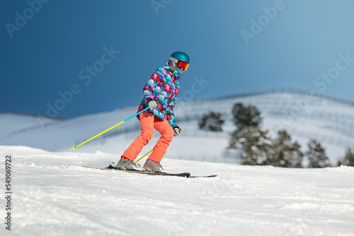Young female skier sliding down the slope on a sunny day at a mountain resort.