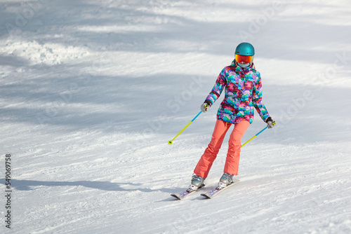 Young female skier learning to slide down the slope on a sunny day at a mountain resort. Copy space.