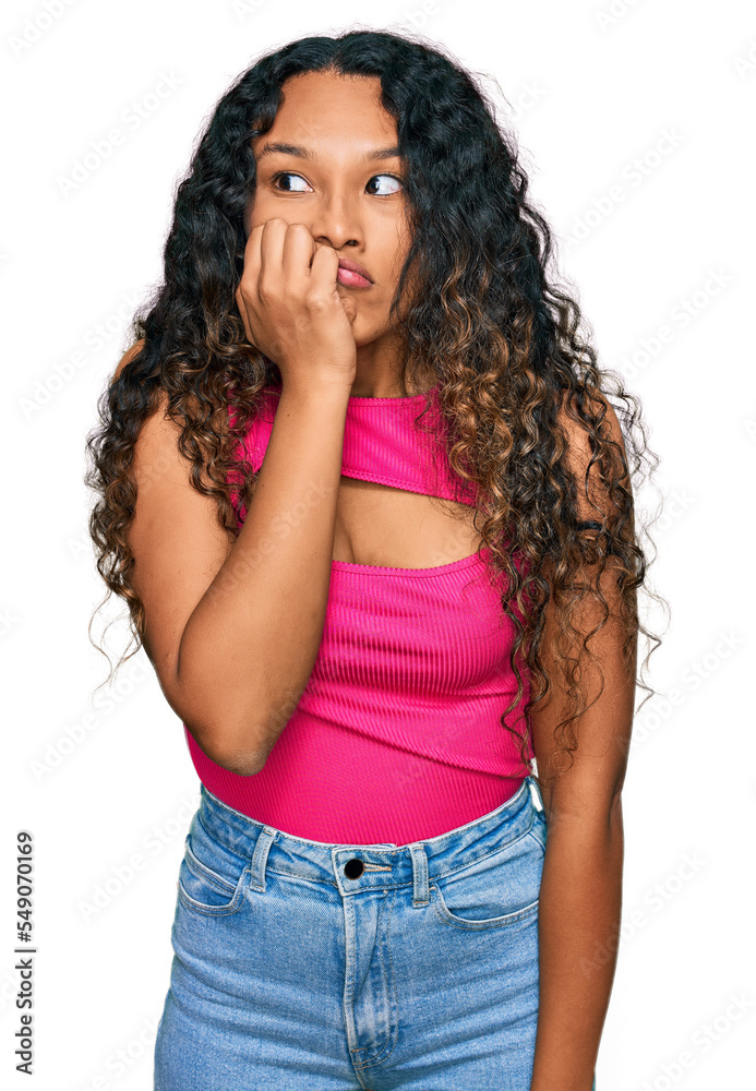 Young hispanic woman with curly hair wearing pink top looking stressed and nervous with hands on mouth biting nails. anxiety problem.