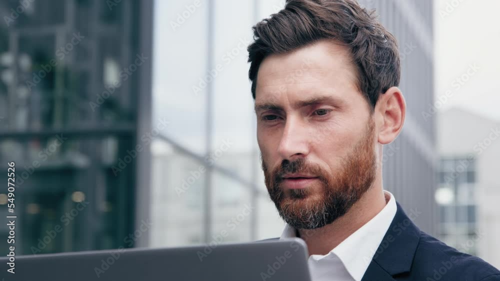 Close-up successful focused pensive man looking at laptop screen professional businessman working online outdoors browsing social network communicates with client on internet creates business project Close-up successful focused pensive man looking at laptop screen professional businessman working online outdoors browsing social network communicates with client on internet creates business project