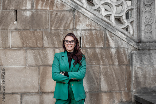 a girl in a green suit and glasses stands near the wall