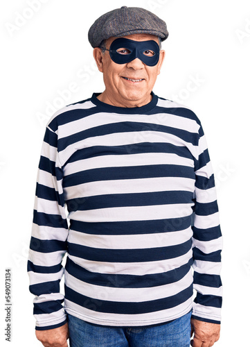 Senior handsome man wearing burglar mask and t-shirt winking looking at the camera with sexy expression, cheerful and happy face.