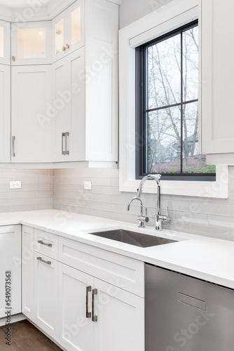 A luxurious modern white kitchen with white cabinets, beautiful granite, and hardwood floors. The kitchen sink has a chrome faucet and a deep, stainless steel tub.