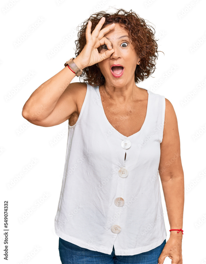 Beautiful middle age mature woman wearing casual white shirt doing ok gesture shocked with surprised face, eye looking through fingers. unbelieving expression. Beautiful middle age mature woman wearing casual white shirt doing ok gesture shocked with surprised face, eye looking through fingers. unbelieving expression.