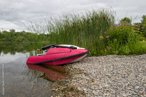 An old jetski parked at a gravel boat launch on a river