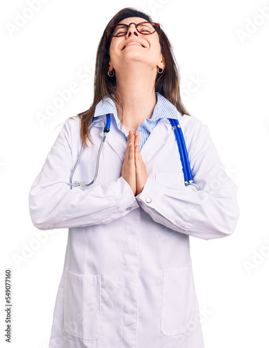Young beautiful woman wearing doctor stethoscope and glasses begging and praying with hands together with hope expression on face very emotional and worried. begging.
