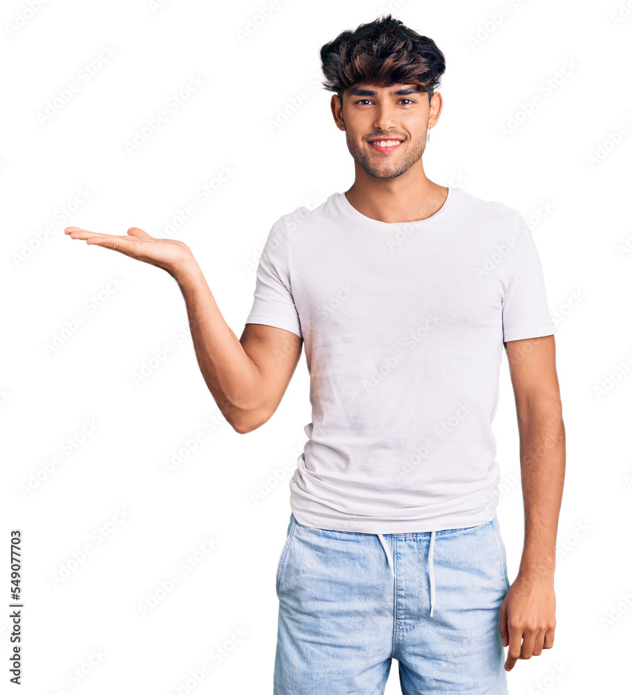 Young hispanic man wearing casual clothes smiling cheerful presenting and pointing with palm of hand looking at the camera. Young hispanic man wearing casual clothes smiling cheerful presenting and pointing with palm of hand looking at the camera.