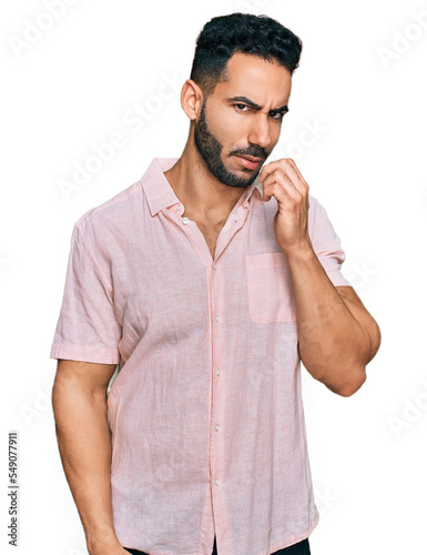 Hispanic man with beard wearing casual shirt looking stressed and nervous with hands on mouth biting nails. anxiety problem.