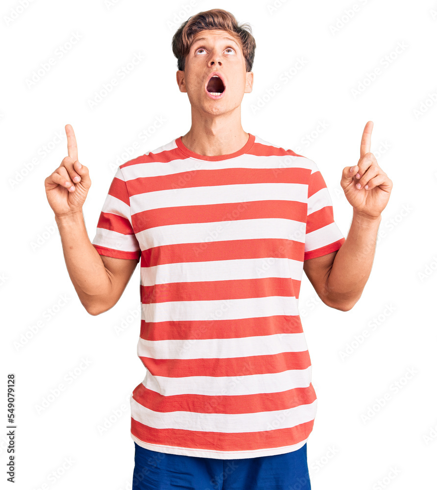 Young handsome man wearing casual clothes amazed and surprised looking up and pointing with fingers and raised arms. Young handsome man wearing casual clothes amazed and surprised looking up and pointing with fingers and raised arms.