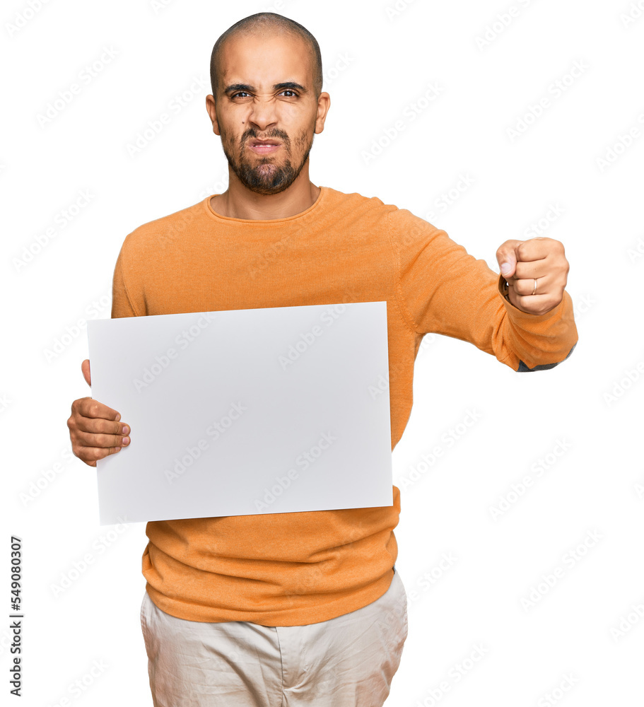 Hispanic adult man holding blank empty banner annoyed and frustrated shouting with anger, yelling crazy with anger and hand raised Hispanic adult man holding blank empty banner annoyed and frustrated shouting with anger, yelling crazy with anger and hand raised