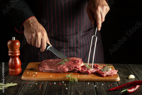 The chef prepares veal with his hands in the kitchen. Menu idea for a restaurant or hotel on a dark background