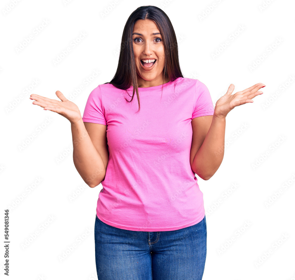 Young beautiful brunette woman wearing casual t-shirt celebrating victory with happy smile and winner expression with raised hands Young beautiful brunette woman wearing casual t-shirt celebrating victory with happy smile and winner expression with raised hands